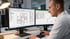 Mann arbeitet an zwei Monitoren mit CAD-Software, zeigt Gebäudegrundrisse und elektrische Schaltpläne.