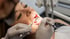 Zahnärztliche Untersuchung einer Patientin mit Mundspiegel und Sonde durch einen Zahnarzt in Handschuhen.