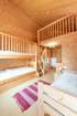 Ein hölzernes Zimmer mit Etagenbett, einem Einzelbett, einer Treppe zu einem Hochbett und einem roten Teppich.