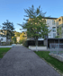 Ein gepflasterter Weg führt zwischen modernen Gebäuden und Bäumen hindurch, mit Gras und Hecken entlang der Seiten.