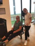 Eine Frau trainiert an einer Beinpresse im Fitnessstudio, während eine Trainerin daneben steht und den Daumen hebt.