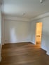 Leeres Zimmer mit Holzboden und weiß gestrichenen Wänden, offener Tür zu einem Badezimmer.
