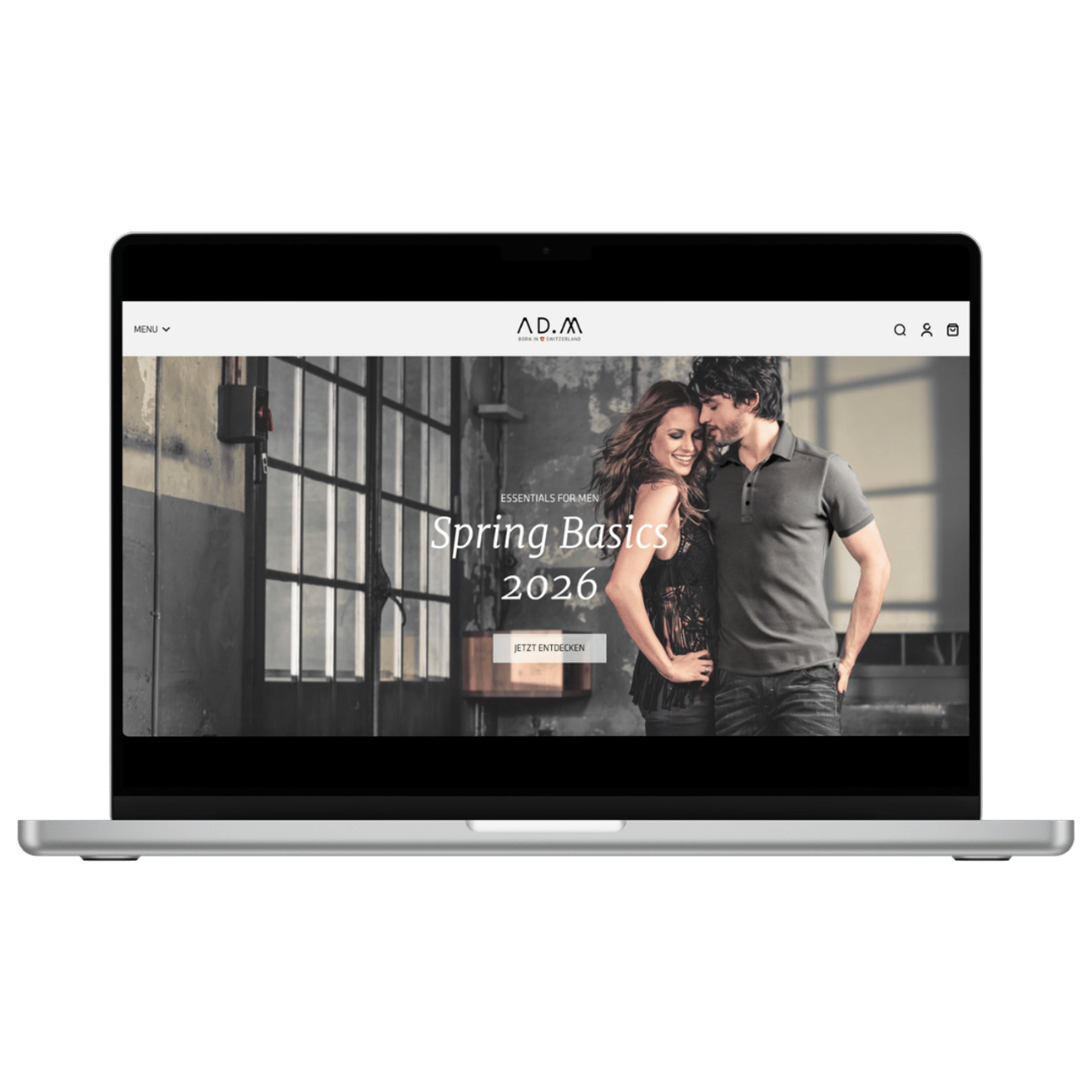Laptop zeigt die A.D.M. Webseite mit einer Frau und einem Mann, die sich umarmen. "Spring Basics 2026" ist zu lesen.