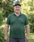Kristoph S., Gärtner bei Volker Möller GalaBau, im grünen Firmenpolo mit Kappe im Garten.