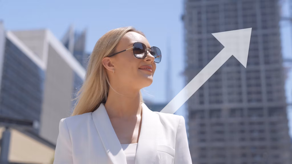Blonde woman in black blazer working on a MacBook in a modern office with a "Real Estate Blondies" banner.
