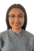 Junge Frau mit dunklem Haar, Brille und grauem Strickpullover lächelt in die Kamera.