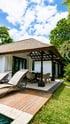 Resort villa with a wooden deck, two lounge chairs, an outdoor dining area, and a lush green lawn.