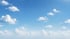 Small white cumulus clouds scattered across a bright blue sky on a clear day.
