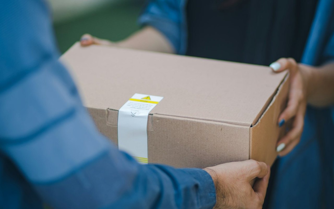 Ein Paket im braunen Versandkarton wird von einer Person an eine andere übergeben