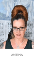 Frau mit rotem Dutt, Brille, schwarzem Oberteil und Anhänger, Text "ANTINA" darunter.