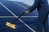 Eine Person reinigt Solarmodule mit einer langen Bürste und Seifenwasser.