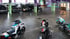 Drei Motorräder stehen vor einer Reihe geparkter schwarzer Autos in einer großen Halle.
