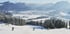 Skifahrer gleiten einen schneebedeckten Hang hinunter, mit einem verschneiten Tal und Bergen im Hintergrund.