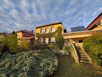 Gelbes Einfamilienhaus mit Solaranlage auf dem Dach, davor der Vorgarten und die Treppe zum Eingang