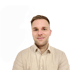 Ein junger Mann mit hellem Hemd lächelt vor einem grünen Hintergrund mit einem weißen Logo.