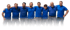 Sieben lächelnde Männer in blauen Hemden und grauen Hosen stehen Schulter an Schulter.