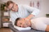 Ein Physiotherapeut massiert den Nacken eines auf einem Behandlungstisch liegenden Mannes.