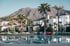 A resort swimming pool with colorful chairs, palm trees, and white buildings, set against a backdrop of mountains.