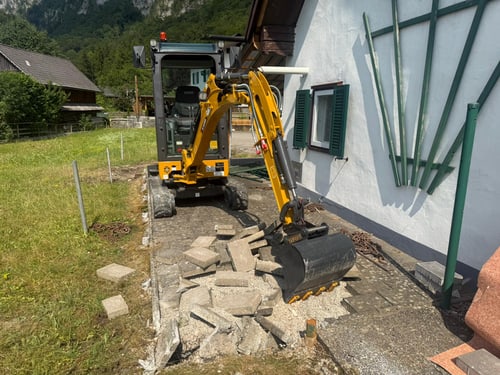 Minibagger hebt alte Pflastersteine neben einem Wohnhaus