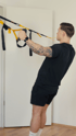 Ein Mann mit Tattoos an den Armen trainiert mit gelben und schwarzen TRX-Bändern.