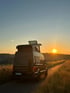 Campervan mit geöffnetem Aufstelldach auf Feldweg bei Sonnenuntergang – individueller Ausbau für stimmungsvolle Vanlife-Erlebnisse in der Abendsonne