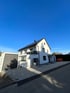 Weißes Einfamilienhaus mit Solarpaneelen auf dem Dach und grauer Garage an der Seite.