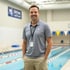 Ein lächelnder Mann in grauem Poloshirt und Khakihosen steht vor einem Schwimmbecken.