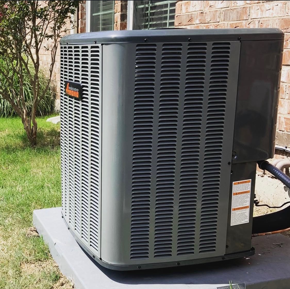 Amana outdoor air conditioning condenser on a concrete pad beside a brick home