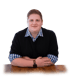 Webdesigner Köthen mit kariertem Hemd und Pullover lehnt mit verschränkten Armen auf einem Holztisch.