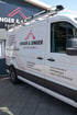 Weißer Transporter der Singer & Singer Dachdeckerei mit Firmenlogo, Kontaktdaten und Dachträger vor einem Firmengebäude.