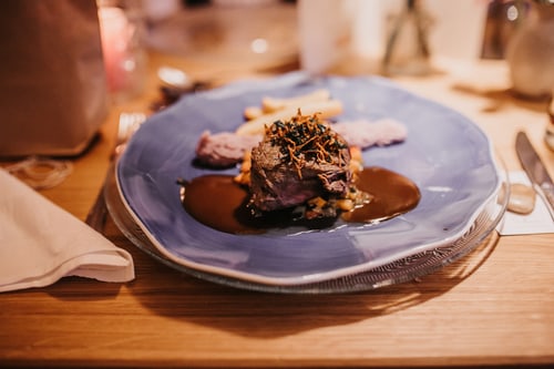 Fein angerichtetes Gericht mit Fleisch, Kartoffelpüree und Jus auf blauem Teller