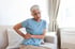Older woman on sofa holding lower back, showing sciatica nerve pain.