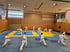 Gruppe von 15 Personen in weißen Kampfsportanzügen trainiert Karate in einer Turnhalle mit blauer und gelber Matte.