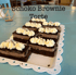 Schoko Brownie Torte: Mehrere Schoko-Brownie-Stücke mit Sahnehauben und Schokostreuseln auf weißer Platte.