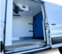 Open side door of a white refrigerated delivery van with a blue divider wall and interior cooling unit.