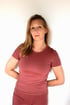 Porträt einer blonden Frau in einem altrosa T-Shirt vor weißem Hintergrund mit hinter dem Rücken verschränkten Armen.