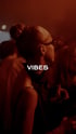 Frau mit Dutt, Brille und schwarzem Oberteil von der Seite, umgeben von anderen Menschen, mit Text "VIBES".