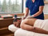 A practitioner in blue scrubs performs acupuncture on a man's back as he lies on a massage table.