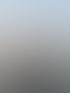 Ein lächelnder Mann mit Brille und schwarzem Pullover steht vor einem ruhigen Gewässer mit hellem Himmel bei Sonnenuntergang.