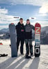 Pascal und Tim stehen mit Snowboards im Schnee vor einer Bergkulisse unter blauem Himmel mit Wolken.