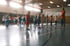 Kinder heben in einer Sporthalle ihre Finger, während ein Trainer in orangefarbenem Shirt vor ihnen steht.