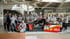 Ein Team steht in einem Autohaus hinter einem rot-schwarzen BMW DTM Rennwagen mit Shell-Logo.