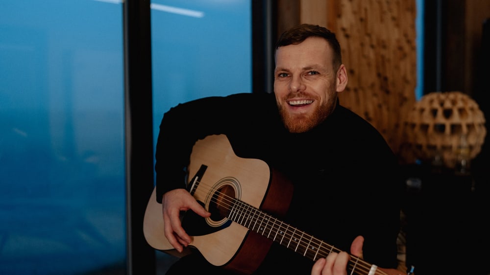 Mann lächelt mit Gitarre in der Hand