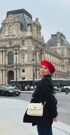 Frau mit roter Baskenmütze und weißer Handtasche vor dem Louvre in Paris.