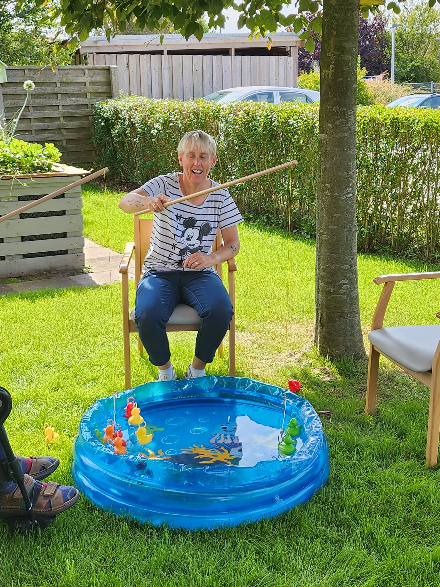 Eine Frau angelt im Garten nach bunten Spielzeugenten in einem kleinen Wasserbecken.