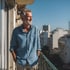 Einer unser zufriedenen Kunden steht auf dem Balkon seiner Eigentumswohnung und schaut an einem sonnigen und wolkenfreien Tag zufrieden nach draußen in die Straße
