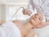 Eine Kosmetikerin führt eine Microneedling-Behandlung im Gesicht einer entspannten Frau in einem hellen Behandlungsraum durch.