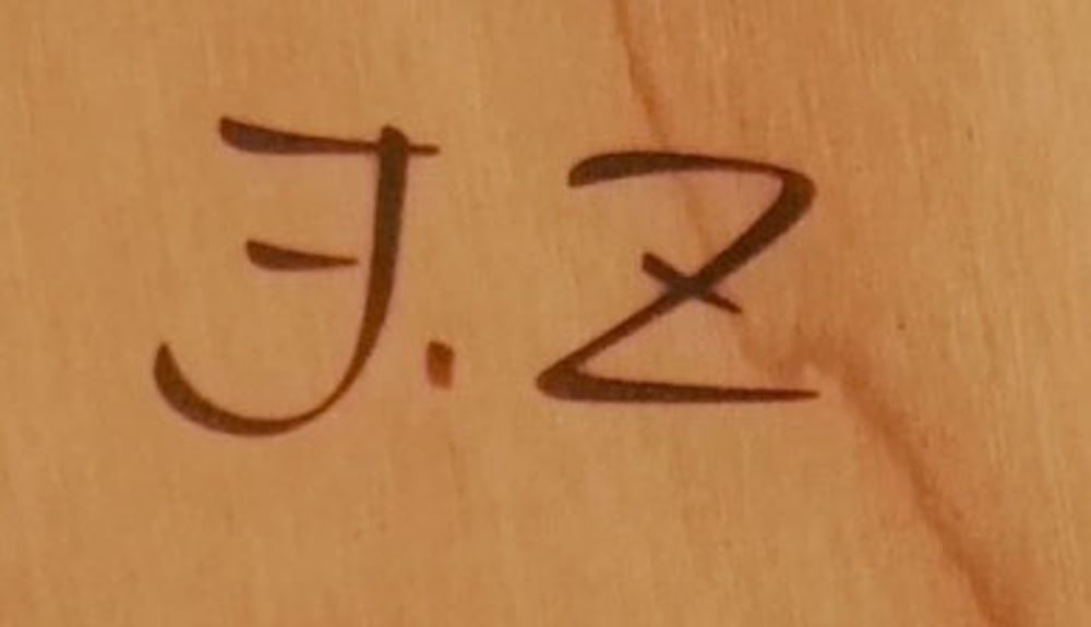 Dunkelbraune Initialen "J. Z" auf hellbraunem Holz.