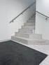 Treppe aus hellem Terrazzo mit Edelstahlgeländer und schwarzem Fußabtreter.