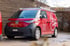Roter VW ID. Buzz Cargo Lieferwagen mit Dachgepäckträger und Virgin Media Logo parkt vor Holzfassade.